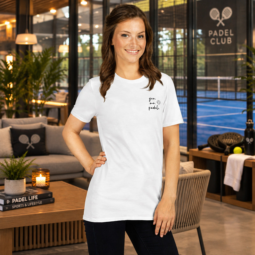 T-Shirt für Padel Tennis Spieler. Eine Frau steht in einer Lounge von einer Padelhalle. Im Hintergrund it ein Padel Tennis Platz zu sehen.